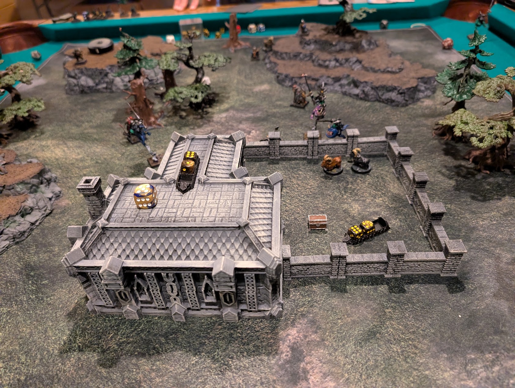 Miniatures and goats spread across a farm battlefield beside a large stone building and enclosed courtyard.